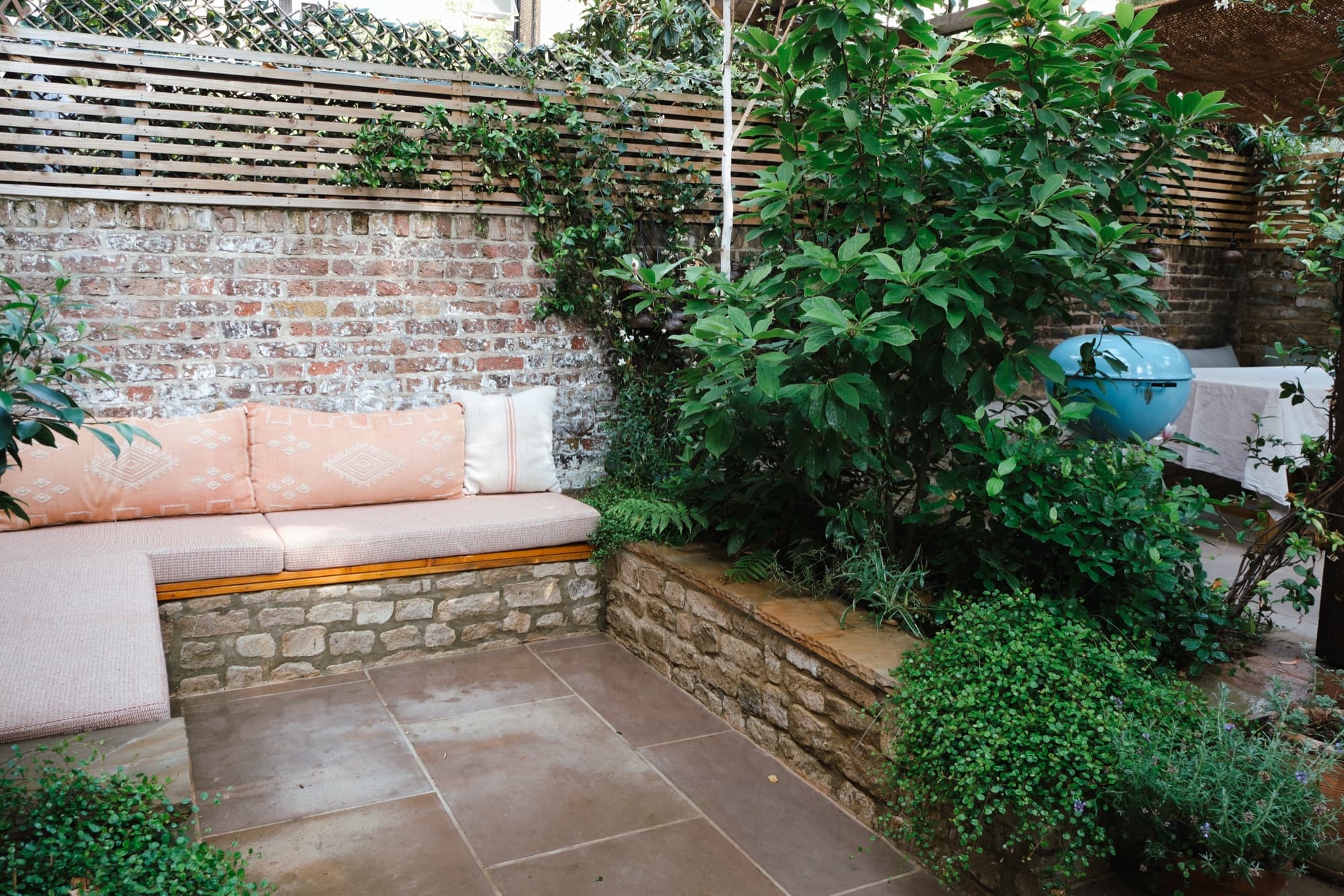 Built-in bench with blush cushions against a reclaimed brick wall in a walled West London garden