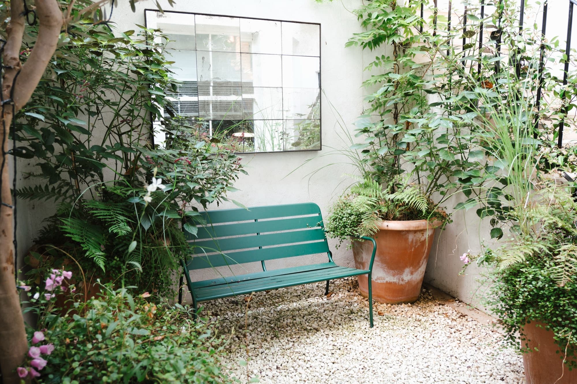Basement courtyard with a green metal bench, antiqued mirror and gravel underfoot