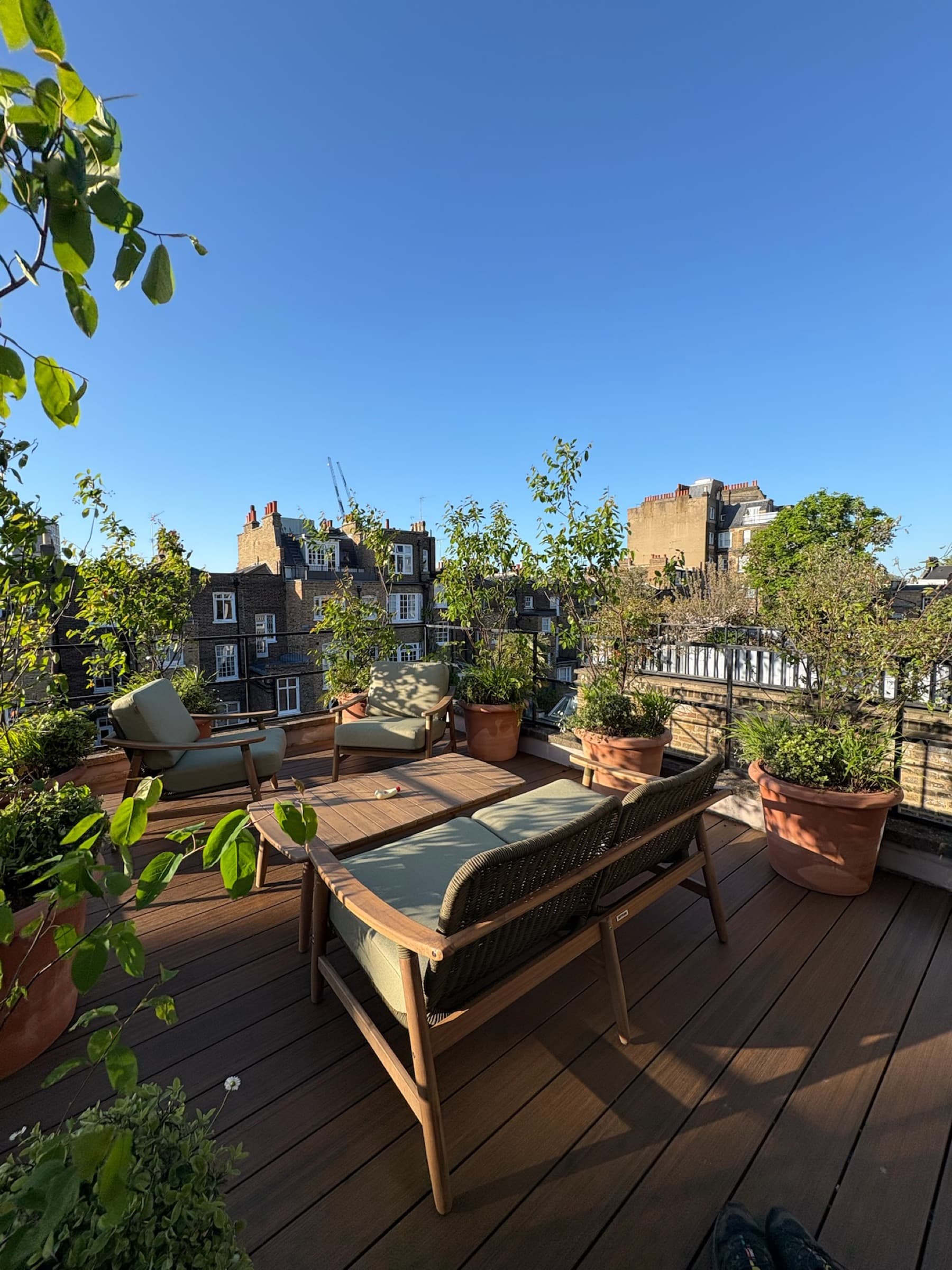 A planted rooftop terrace with timber furniture and terracotta pots above the West London skyline
